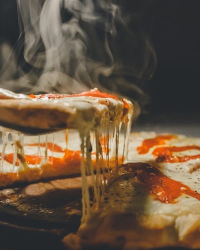 Dampfend-heißes Stück Pizza mit langen Käsefäden vor einem dunklen Hintergrund